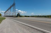 an empty highway under a power line under blue skies above the street and bushes of green