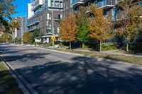 a street lined with tall buildings and trees in the fall, on a clear day