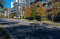 a street lined with tall buildings and trees in the fall, on a clear day