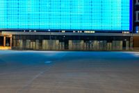 an empty parking lot in front of a brightly lit building with blue lights at night