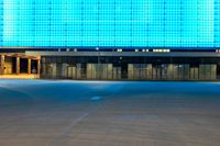 an empty parking lot in front of a brightly lit building with blue lights at night