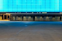 an empty parking lot in front of a brightly lit building with blue lights at night