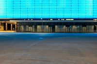 an empty parking lot in front of a brightly lit building with blue lights at night