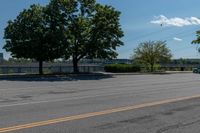 a black car driving down an empty street by some trees and bushes on either side