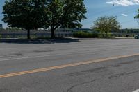 a black car driving down an empty street by some trees and bushes on either side