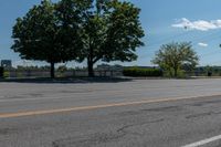 a black car driving down an empty street by some trees and bushes on either side