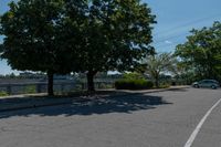 a black car driving down an empty street by some trees and bushes on either side