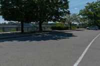 a black car driving down an empty street by some trees and bushes on either side