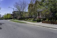 empty street lined with residential buildings and bushes in the sidewalk next to curb with trees, lawn and lawn