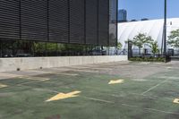 a parking lot with yellow arrows painted on it and buildings in the background there are multiple trees and grass