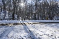 a road covered by snow with trees and the sun shining on the road behind it