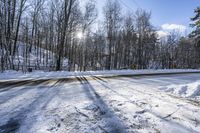 a road covered by snow with trees and the sun shining on the road behind it