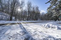 a road covered by snow with trees and the sun shining on the road behind it