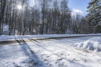 a road covered by snow with trees and the sun shining on the road behind it