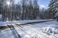 a road covered by snow with trees and the sun shining on the road behind it