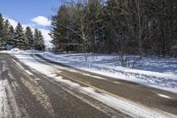 an empty road and some trees on the side of it in snow, with a white truck stuck in the middle of the snow