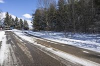 an empty road and some trees on the side of it in snow, with a white truck stuck in the middle of the snow