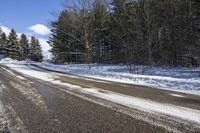 an empty road and some trees on the side of it in snow, with a white truck stuck in the middle of the snow