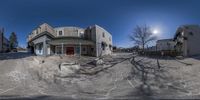 a fisheye view of an empty building and the surrounding street are snow covered with sand