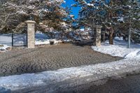 there is a small driveway covered in snow near a tree lined driveway with two gates