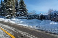 a rural road near some trees in the snow and a building on the side of it