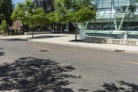 a building with glass is seen in the distance behind it is trees on both sides of a street