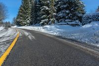 a road near the side of a hill covered with snow and evergreen trees next to the road