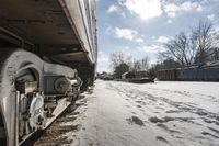 an old rail car is parked on the tracks in the snow by railroad cars with a sky background