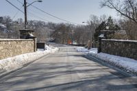 the road is lined with snow and brick along the side of a road is the bridge and a gate,