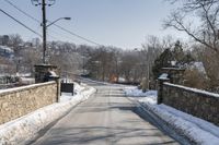 the road is lined with snow and brick along the side of a road is the bridge and a gate,