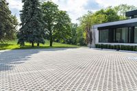 the driveway of this home has a grid pattern in it and trees, hedges, bushes and buildings behind