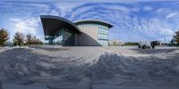 this is a fisheye panoramic photo of a building with circular shapes in front and people walking on the side walk in front