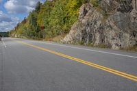 an asphalt road with multiple lanes and yellow markings in front of a cliff face on the side of it