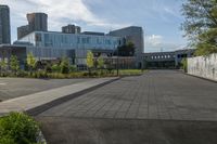 a city street surrounded by grass and tall buildings at the end of a street there is a paved pathway in front of the building