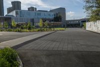 a city street surrounded by grass and tall buildings at the end of a street there is a paved pathway in front of the building