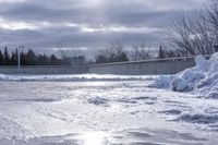 there is a large pile of snow next to a frozen road with a bridge behind it