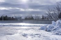 there is a large pile of snow next to a frozen road with a bridge behind it