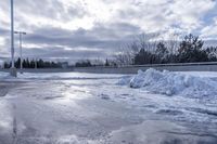 there is a large pile of snow next to a frozen road with a bridge behind it