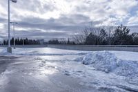 there is a large pile of snow next to a frozen road with a bridge behind it