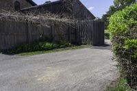 an empty driveway leads to two large barn buildings on one side and a fenced in yard behind it