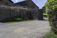 an empty driveway leads to two large barn buildings on one side and a fenced in yard behind it