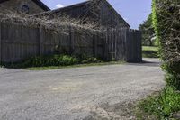 an empty driveway leads to two large barn buildings on one side and a fenced in yard behind it