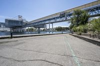 there is a concrete sidewalk and some bridge that spans the river's edge with a blue sky