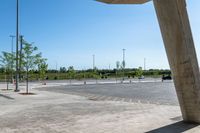 an empty parking lot under a blue sky with trees in the corner of it to the left