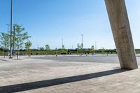 an empty parking lot under a blue sky with trees in the corner of it to the left