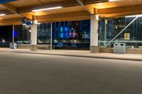 a street at night with cars passing by the parking meters, and the lights are turned on