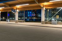 a street at night with cars passing by the parking meters, and the lights are turned on