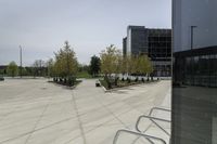 a large plaza with metal benches and tables and trees, on the outside of a tall building