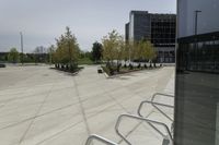 a large plaza with metal benches and tables and trees, on the outside of a tall building