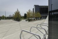 a large plaza with metal benches and tables and trees, on the outside of a tall building